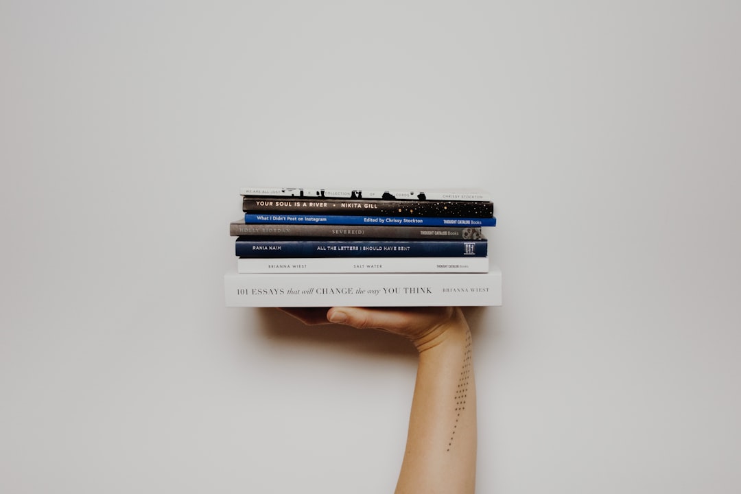 Woman with a tattoo holding up a stack of books.